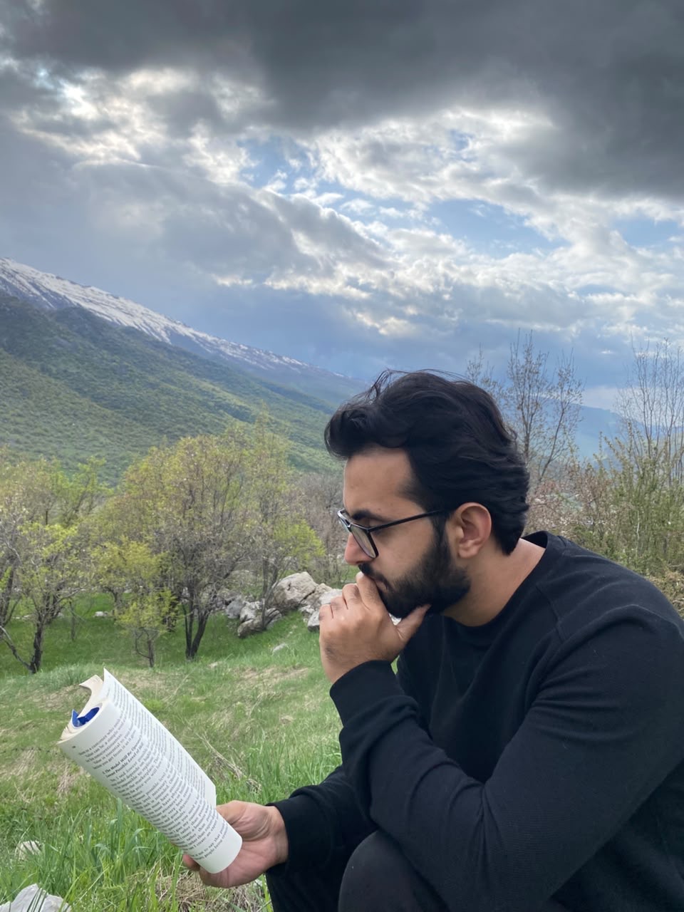Shamil Lateef reading outdoors, mountains behind him